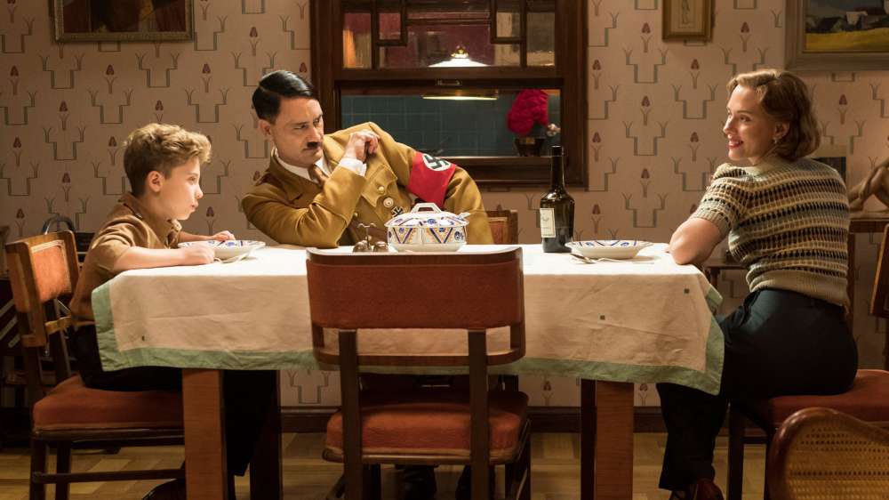First still from the set of WW2 satire, JOJO RABIT. (From L-R): Jojo (Roman Griffin Davis) has dinner with his imaginary friend Adolf (Writer/Director Taika Waititi), and his mother, Rosie (Scarlet ...